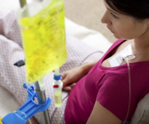 Pregnant woman in a hospital bed receiving IV fluids, with a yellow IV bag above her.