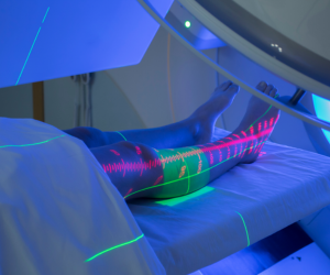 Person lying on a treatment bed under blue UV lighting, with neon laser lines visible on their legs